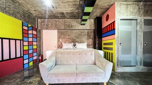 A bedroom with a large bed, a sofa, a door, and a wall with a colorful geometric pattern. - D522 Hostel at Kiener Hills - Near Cebu Airport (Lapu-Lapu)