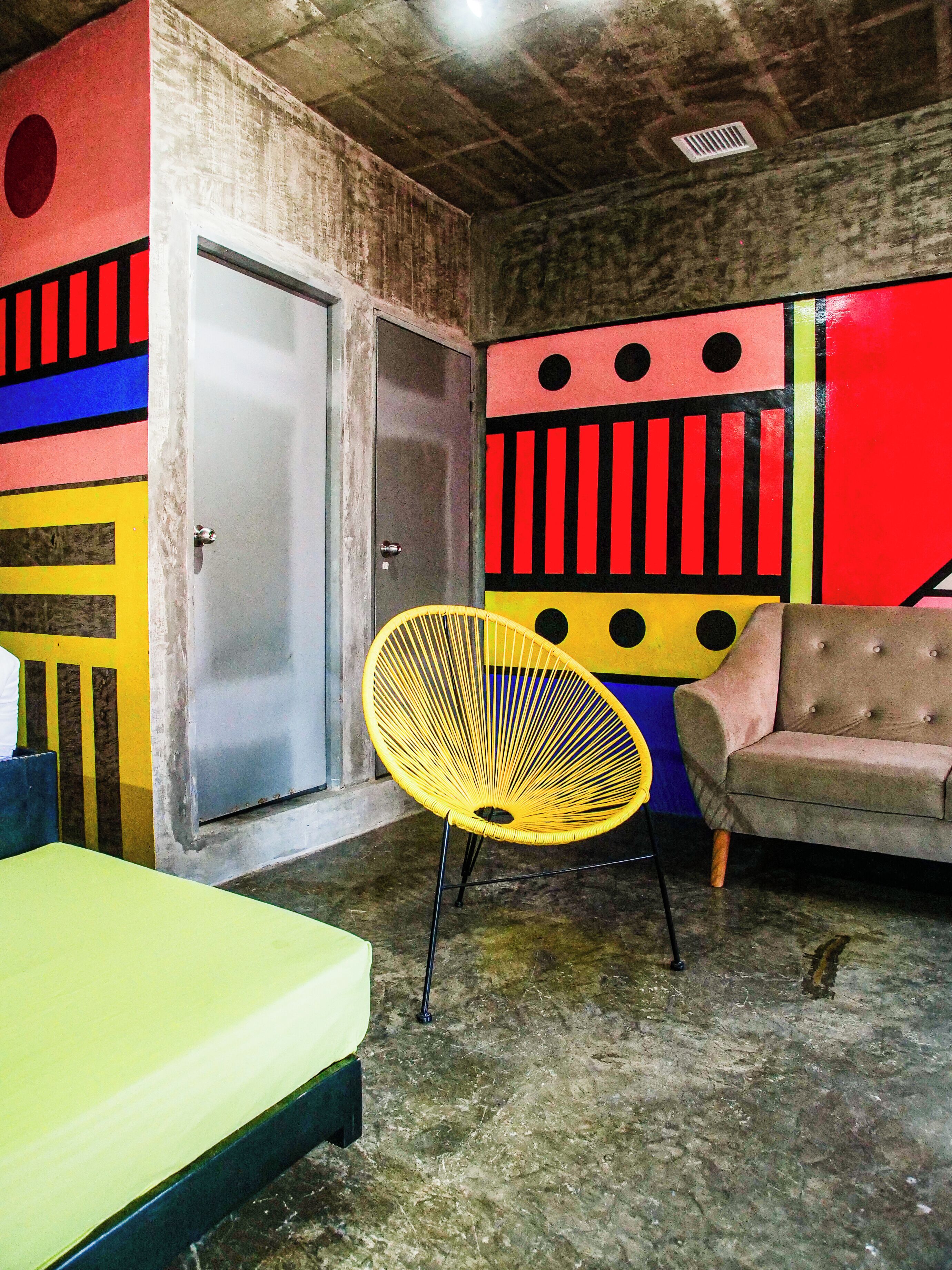 Une pièce avec un lit, une chaise jaune, un canapé et une porte.