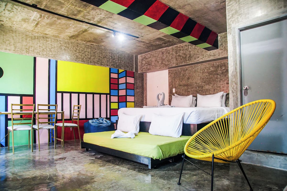 A room with a bed, a yellow chair, and a small table with chairs.