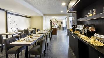 Un comedor moderno con mesas largas, sillas negras y un mostrador de buffet con diversos alimentos.