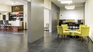 Un vestíbulo de hotel con mostrador de recepción, zona de bar y área de descanso con sillas amarillas.