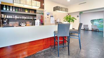 Zona de recepción con mostrador, taburetes, cafetera y una planta en la pared.