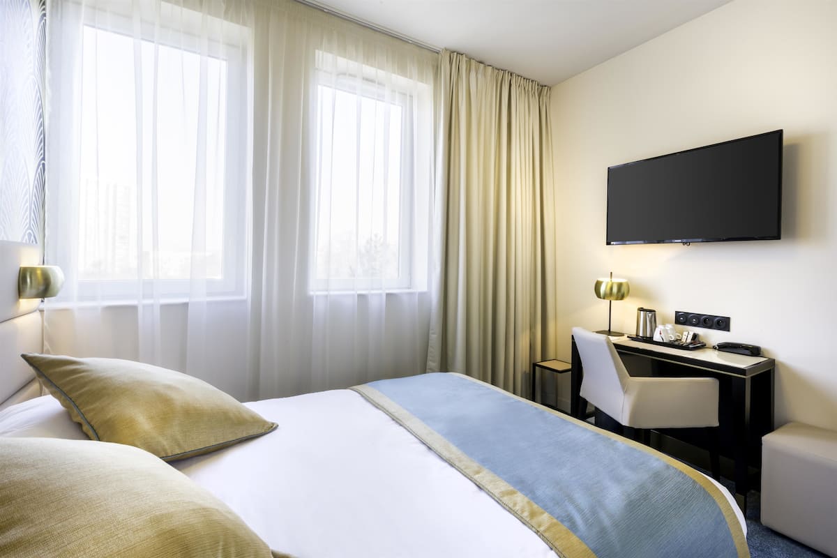 A hotel room with a bed, a desk, a chair, a television, and curtains.