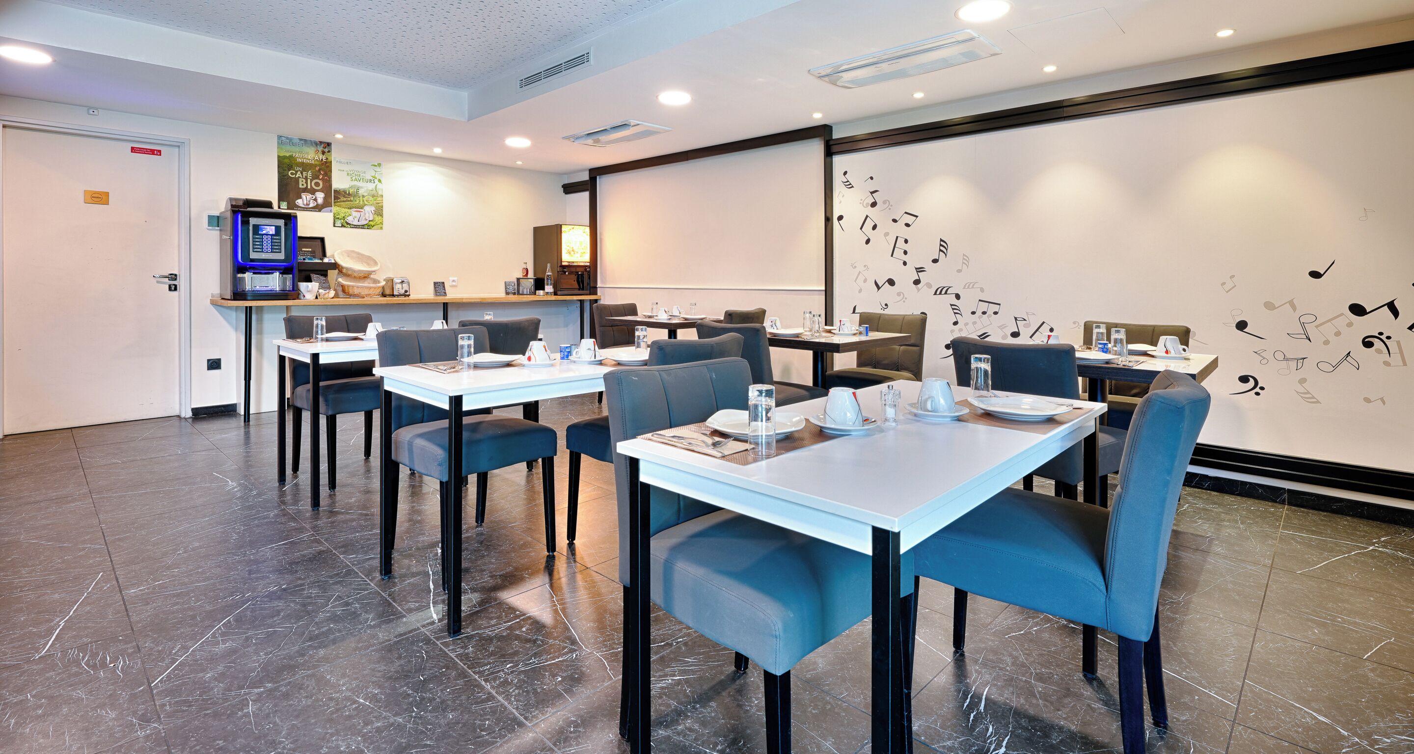 Uma área de jantar moderna com mesas, cadeiras, uma máquina de café e uma tela de projeção na parede.