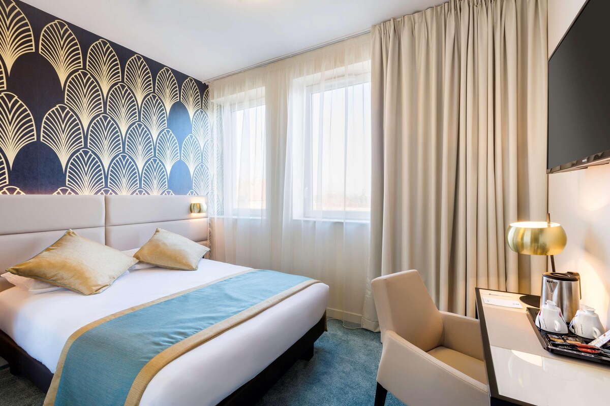 Habitación de hotel con una cama grande, un escritorio con lámpara, una silla y un adorno en la pared.