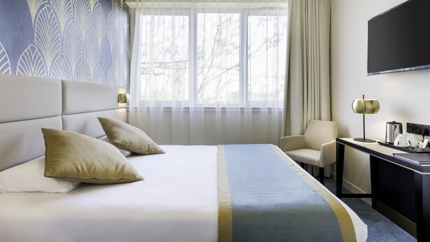 Habitación de hotel con una cama grande, dos almohadas, un escritorio con lámpara, una silla y un televisor en la pared.