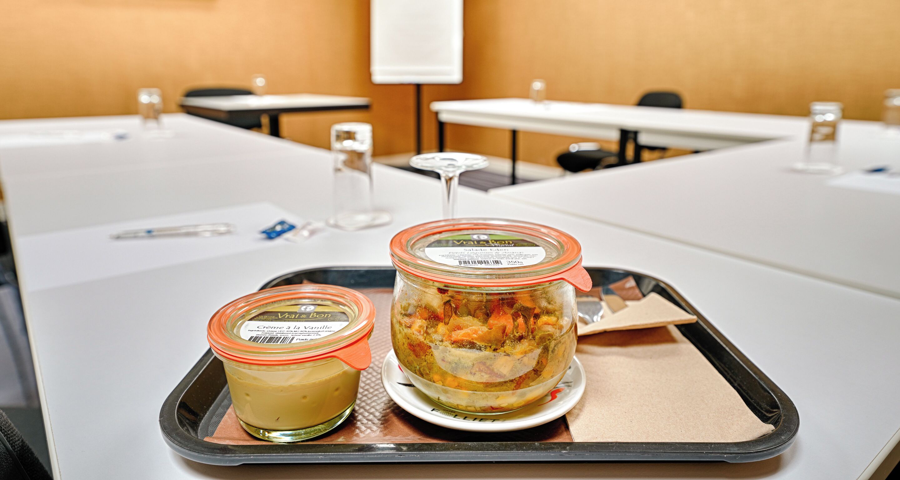 Un plateau avec deux pots de nourriture est posé sur une table dans une salle de conférence.