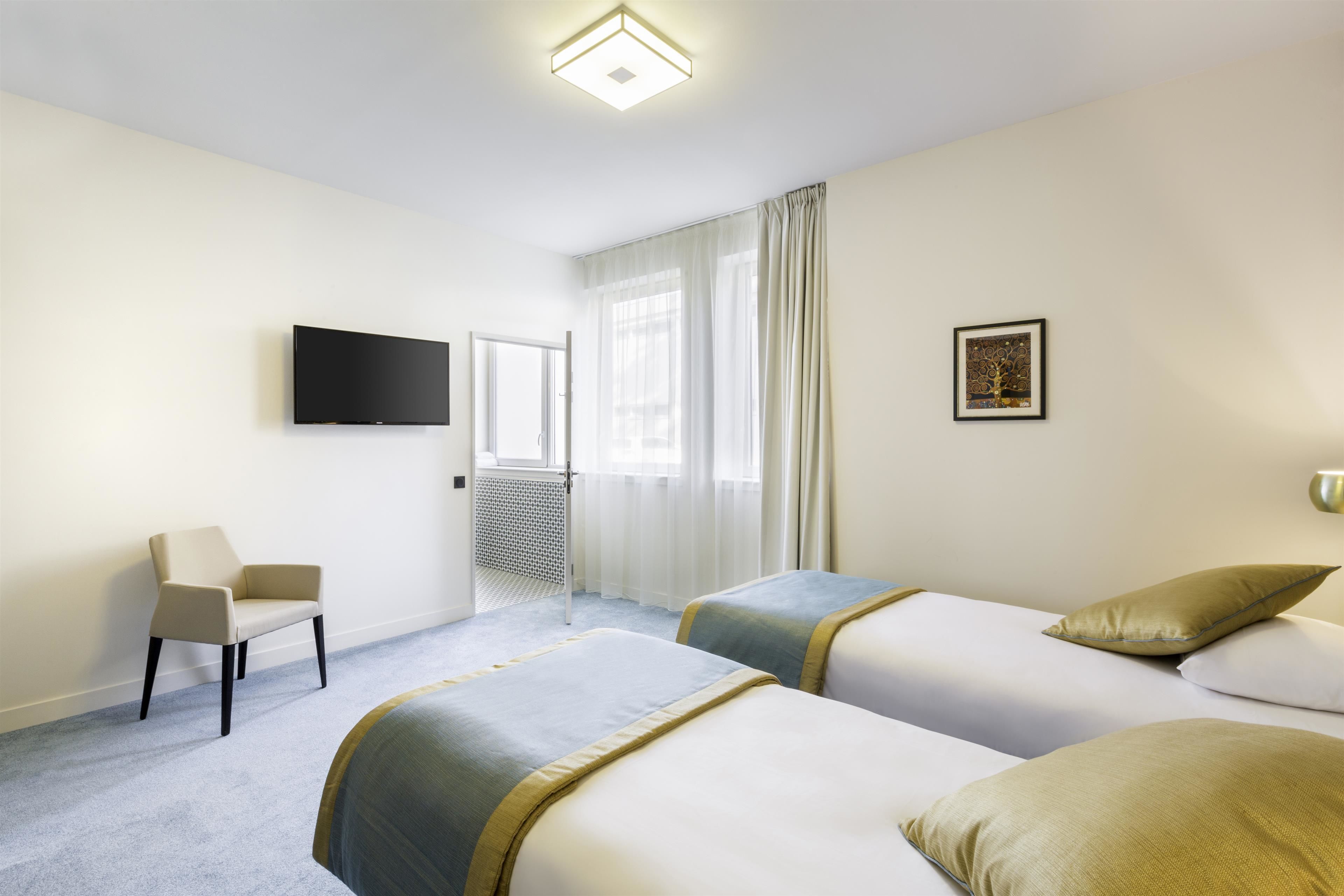A hotel room with two beds, a flat-screen TV, a chair, and a window with curtains.