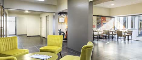 A spacious lobby with yellow chairs and a round table, a staircase, and a view of the outside.