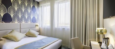 A hotel room with a large bed, a desk with a lamp, and a view of the city through the window.
