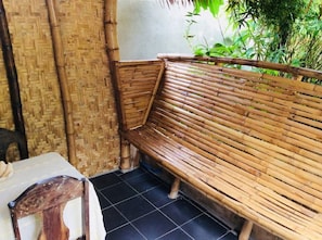 A bamboo bench in a corner with a woven wall and a tiled floor.