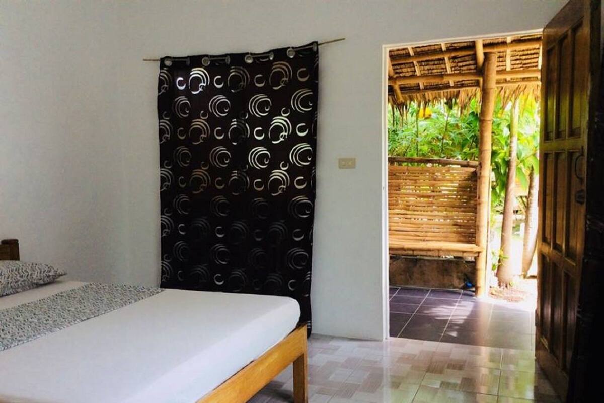 A bedroom with a bed, a black curtain with a circular pattern, and a view of a bamboo structure outside.
