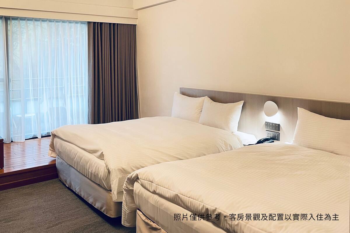 A hotel room with two beds, a desk, and a view of the outdoors.