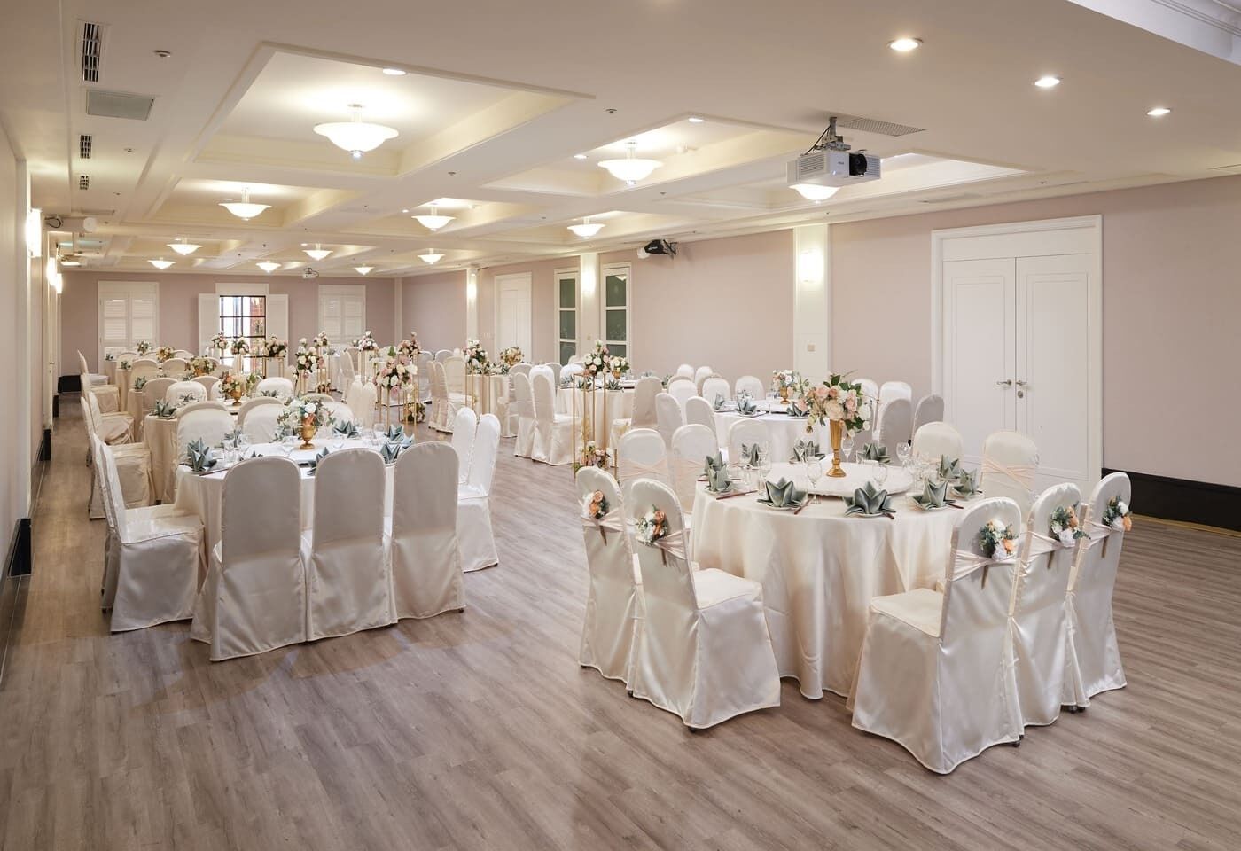 A large banquet hall with multiple round tables, white chairs, and floral centerpieces.
