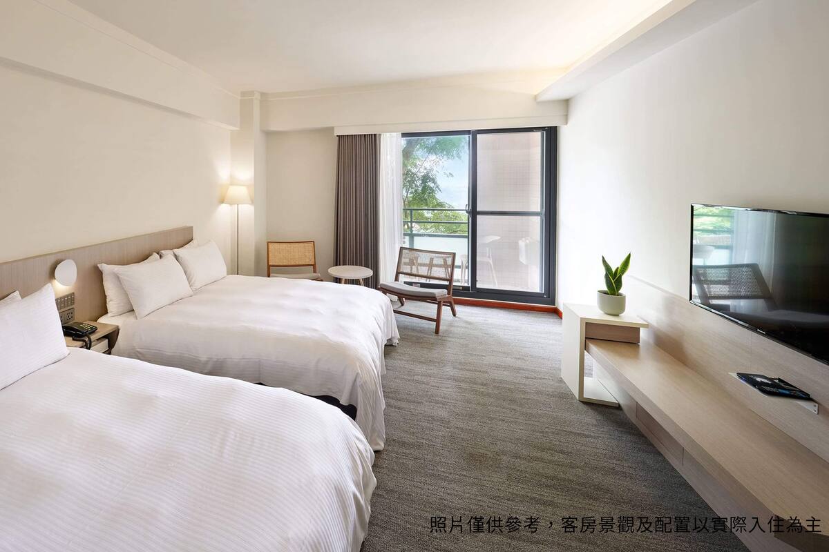 A hotel room with two beds, a TV, a small table, and a chair.