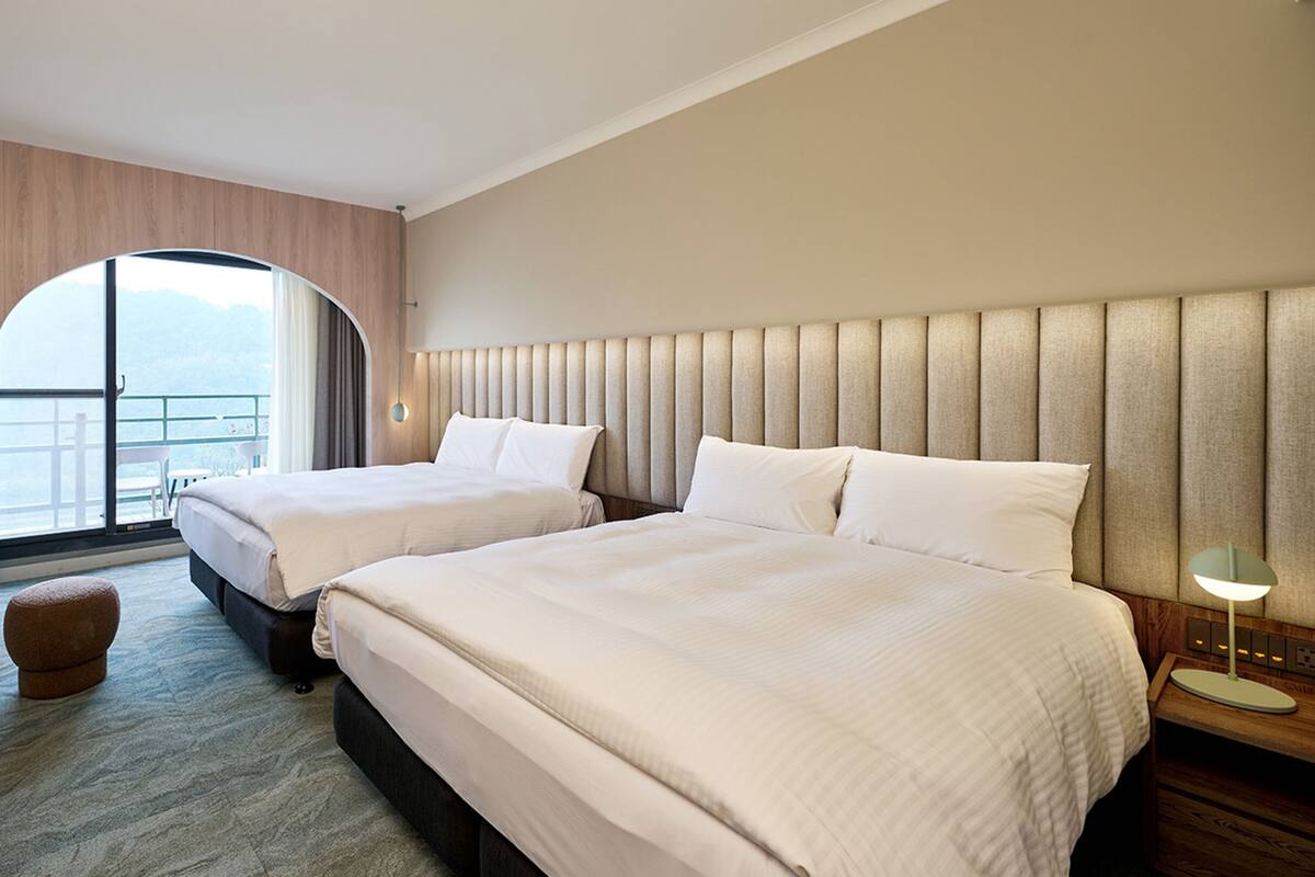 A hotel room with two beds, a TV, a small table, and a view of the sea.