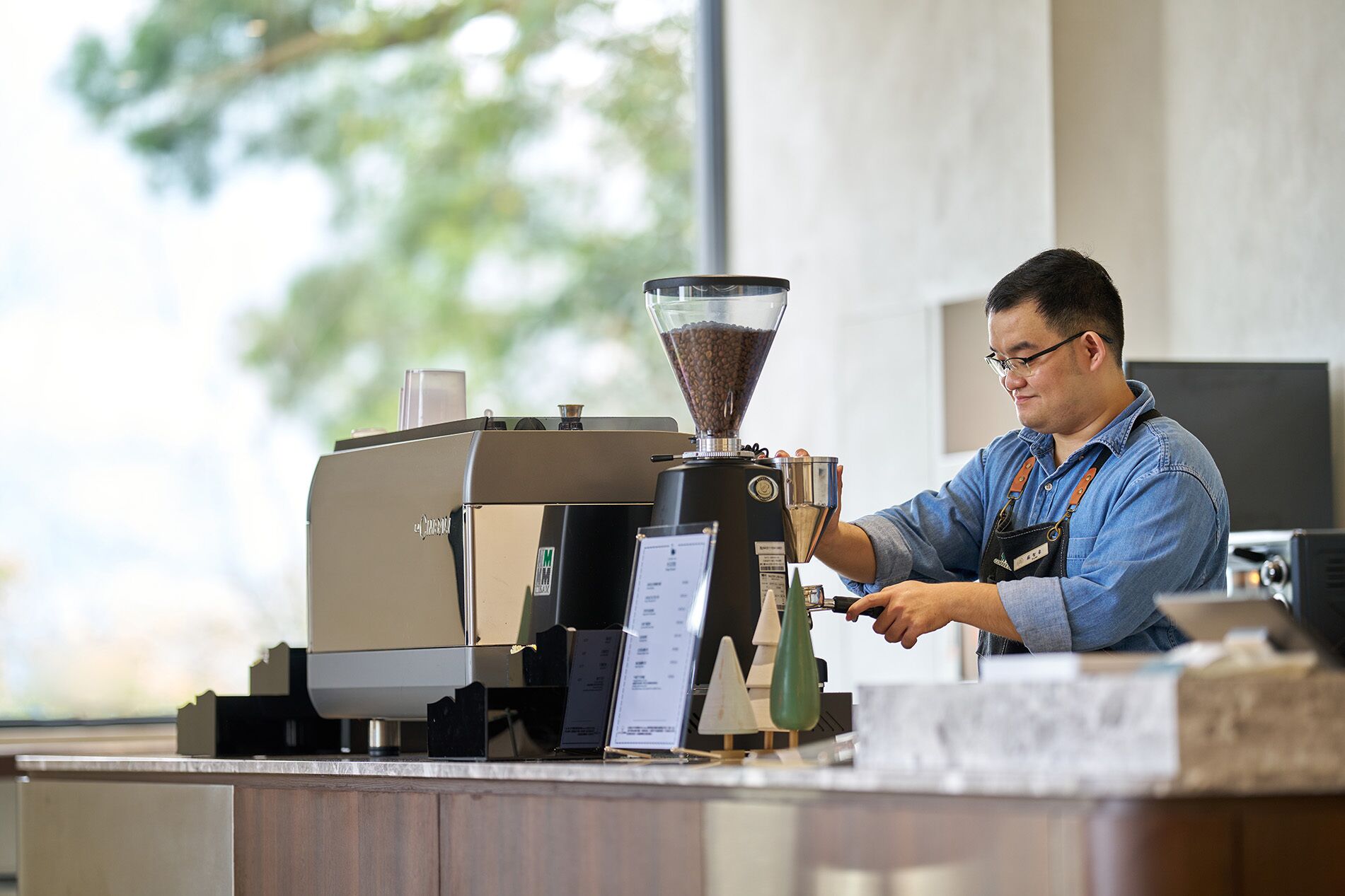 A person operating a coffee machine at a counter with a menu display.