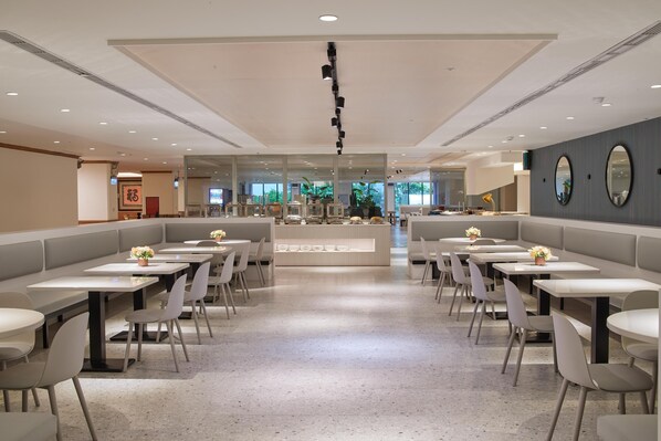 Un restaurante moderno con asientos tipo cabina y mesas redondas, que cuenta con una barra central y flores decorativas.