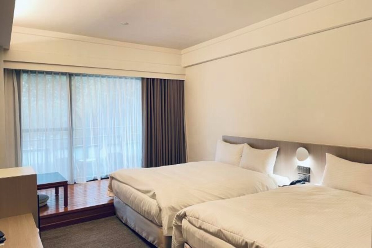 A hotel room with two beds, a desk, and a window with curtains.