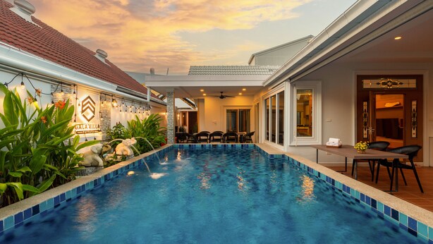 A swimming pool with a tiled edge, surrounded by greenery and a covered patio area. - Gala Villa Pattaya (Pattaya)