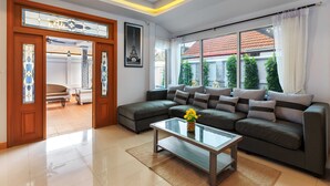 A modern living room with a sectional sofa, a glass coffee table, and a view of the outside. - Gala Villa Pattaya (Pattaya)