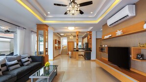 A modern living room with a sofa, coffee table, TV, and kitchen area. - Gala Villa Pattaya (Pattaya)