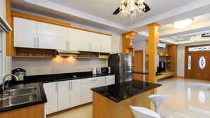 A modern kitchen with white cabinets, a black countertop, stainless steel appliances, and a chandelier. - Gala Villa Pattaya (Pattaya)