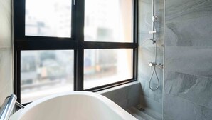A modern bathroom with a bathtub, a shower, and a window providing a view of the cityscape.