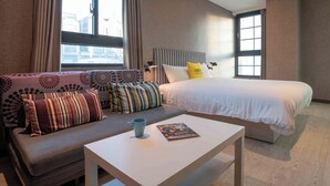 A hotel room with a bed, a sofa, a coffee table, and a window with curtains.