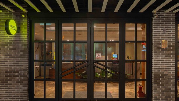 A hotel entrance with a glass door, a neon sign, and a brick wall.
