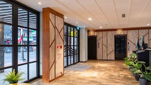 A hotel lobby with wooden paneling, a reception desk, a staircase, and a view of the street outside.