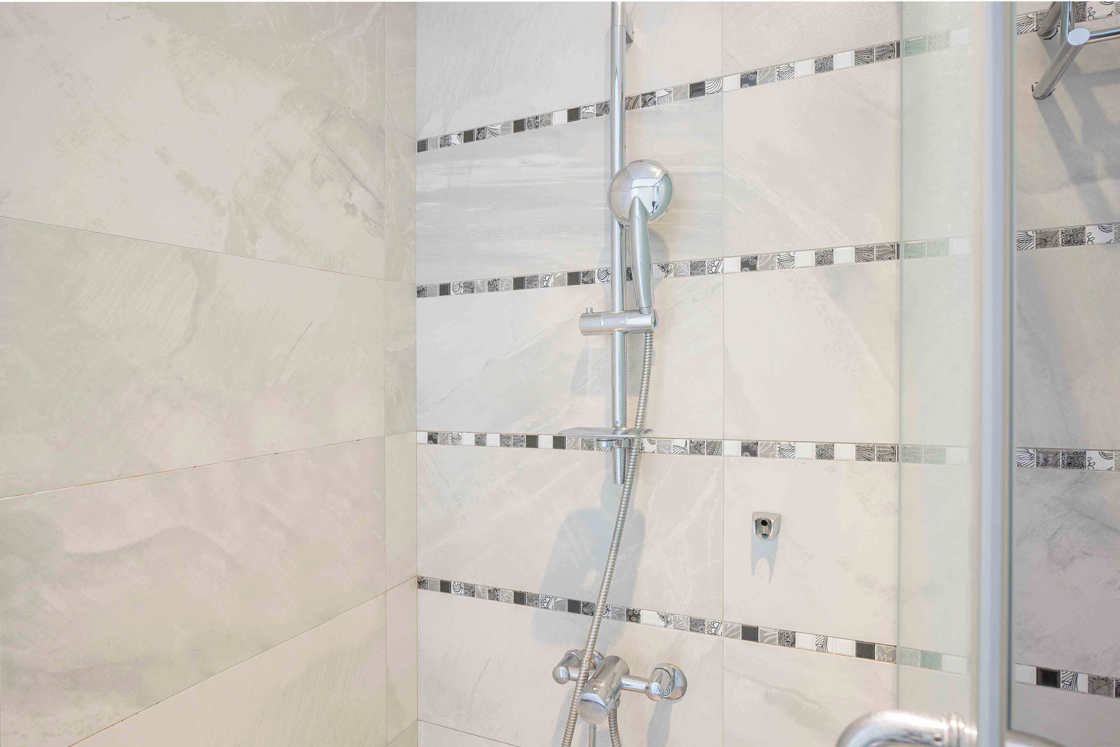A shower with a chrome hose and wall-mounted controls.