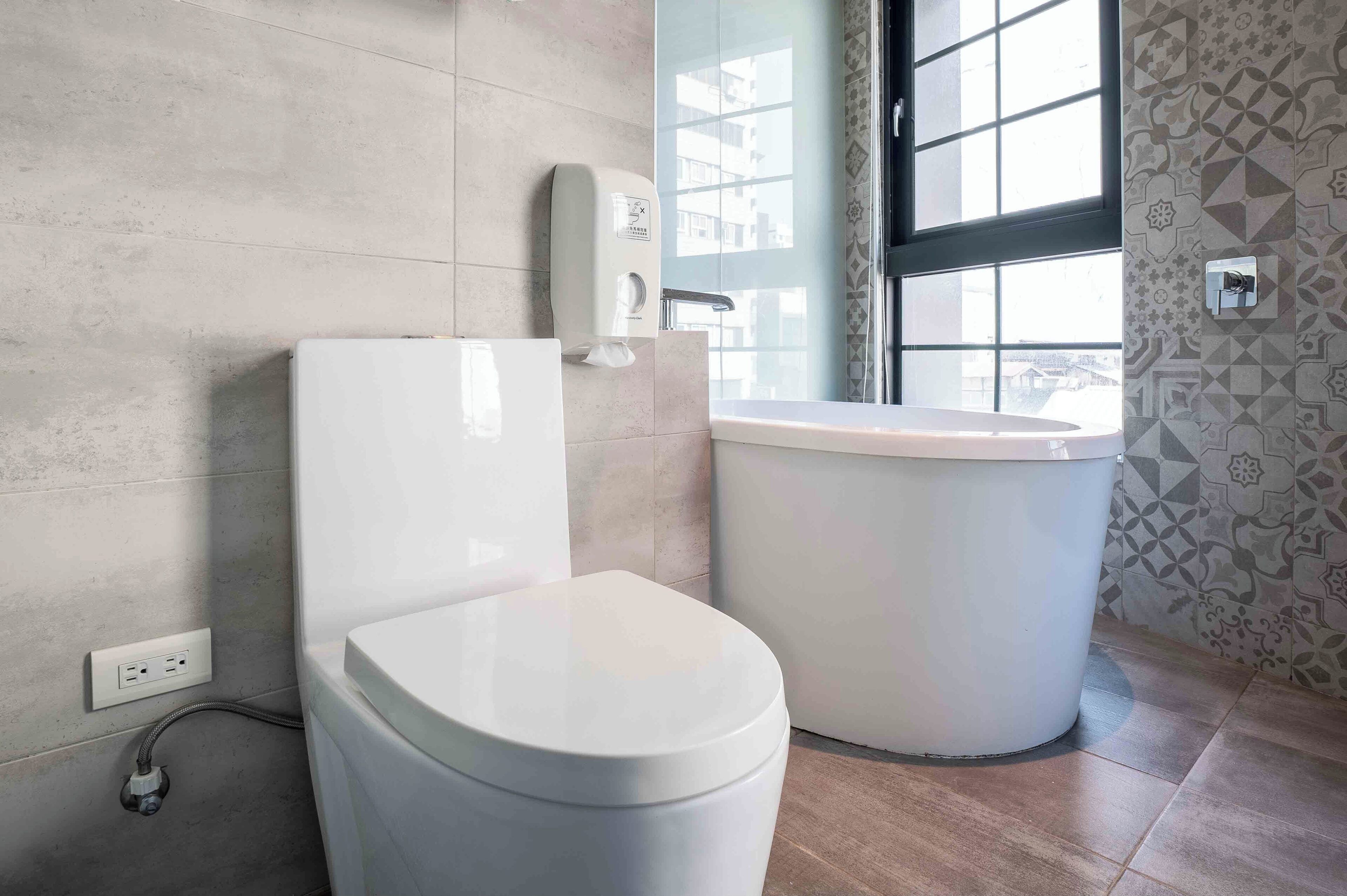 A modern bathroom with a toilet, bidet, and a window.