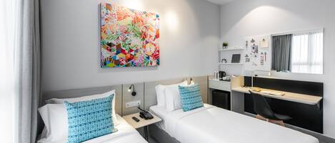 A modern hotel room with two beds, a desk, a chair, a large abstract painting, and a wall-mounted board with photos and notes.