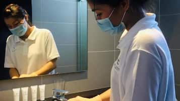 Una persona in divisa bianca in piedi davanti a un lavandino in un bagno con uno specchio sopra.