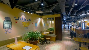 Un interior de restaurante con mesas de madera, plantas en macetas y una pared con texto e ilustraciones.