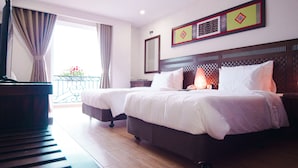 Habitación de hotel con dos camas, un piano, un balcón con flores y un adorno en la pared.