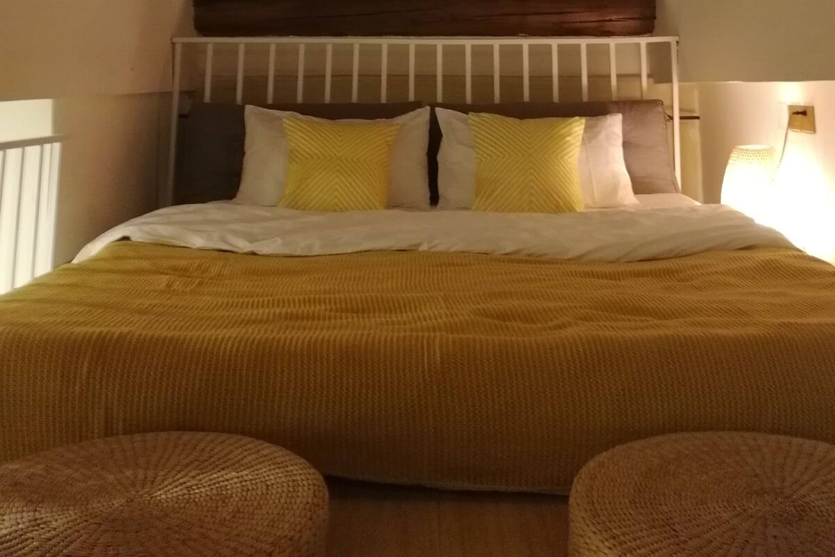 A bedroom with a sloped ceiling, wooden beams, a bed with a white headboard, and two bedside tables with lamps.