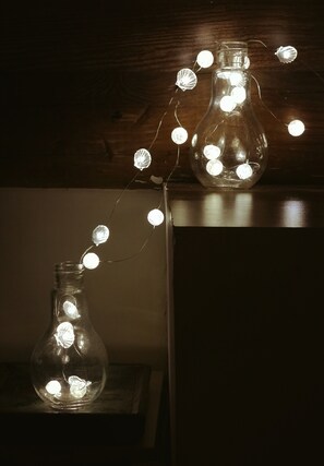 Dos botellas de vidrio transparente con luces de cadena en su interior, sobre una superficie de madera.