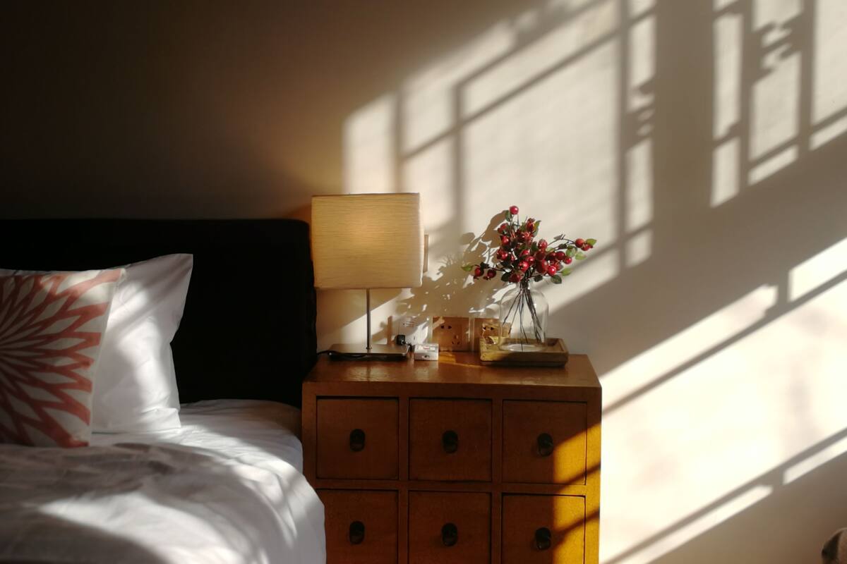 A neatly made bed with a pillow, a bedside table with a lamp, and a vase with red berries.