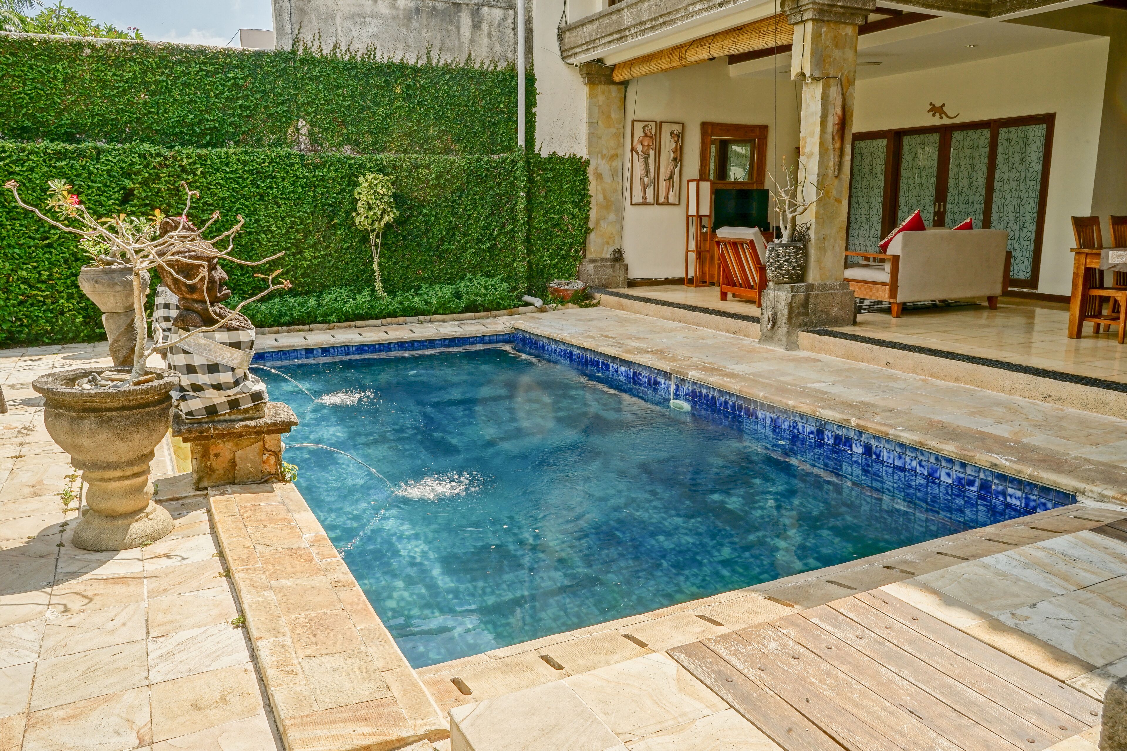 A swimming pool with a tiled edge, surrounded by a stone deck. There are potted plants and a stone sculpture near the pool.