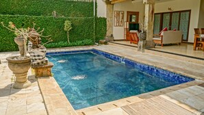 A swimming pool with a tiled edge, surrounded by a stone deck. There are potted plants and a stone sculpture near the pool. - Baliana Villa Batu Belig (Seminyak)