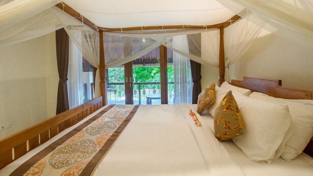A bedroom with a canopy bed, a patterned rug, and a view of greenery outside. - Baliana Villa Batu Belig (Seminyak)