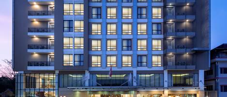 Un hotel moderno con un llamativo letrero 'Swiss-bellinn', varios balcones y un área de entrada bien iluminada.