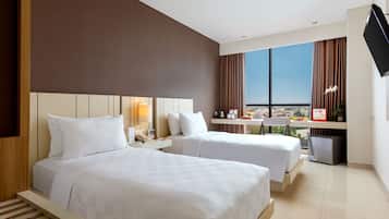 A hotel room with two beds, a desk, a chair, a TV, and a window with a city view.