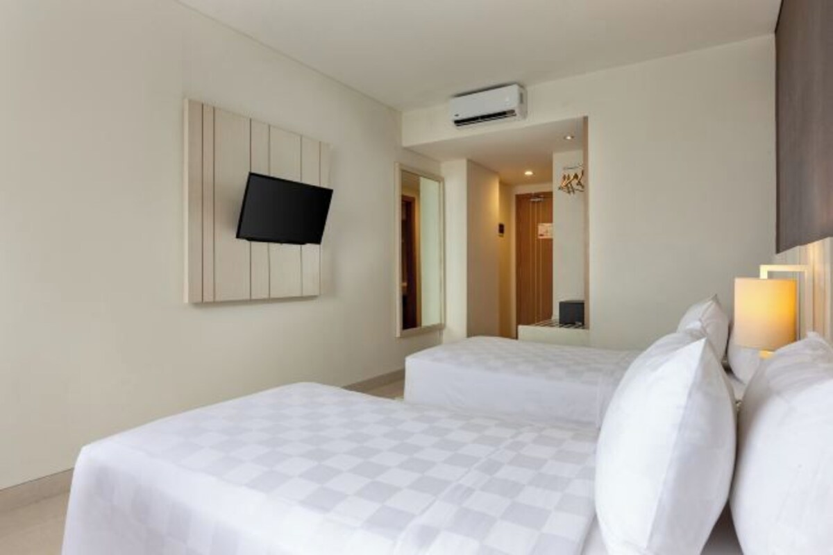 A hotel room with two beds, a flat-screen TV mounted on the wall, an air conditioning unit, and a mirror.