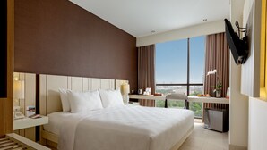 A hotel room with a large bed, a desk, a television, and a view of the city.