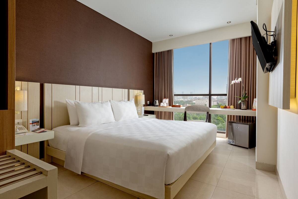 Habitación de hotel con una cama grande, un escritorio, un televisor y vistas a la ciudad.
