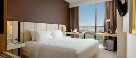 A hotel room with a large bed, a desk, a television, and a view of the city.