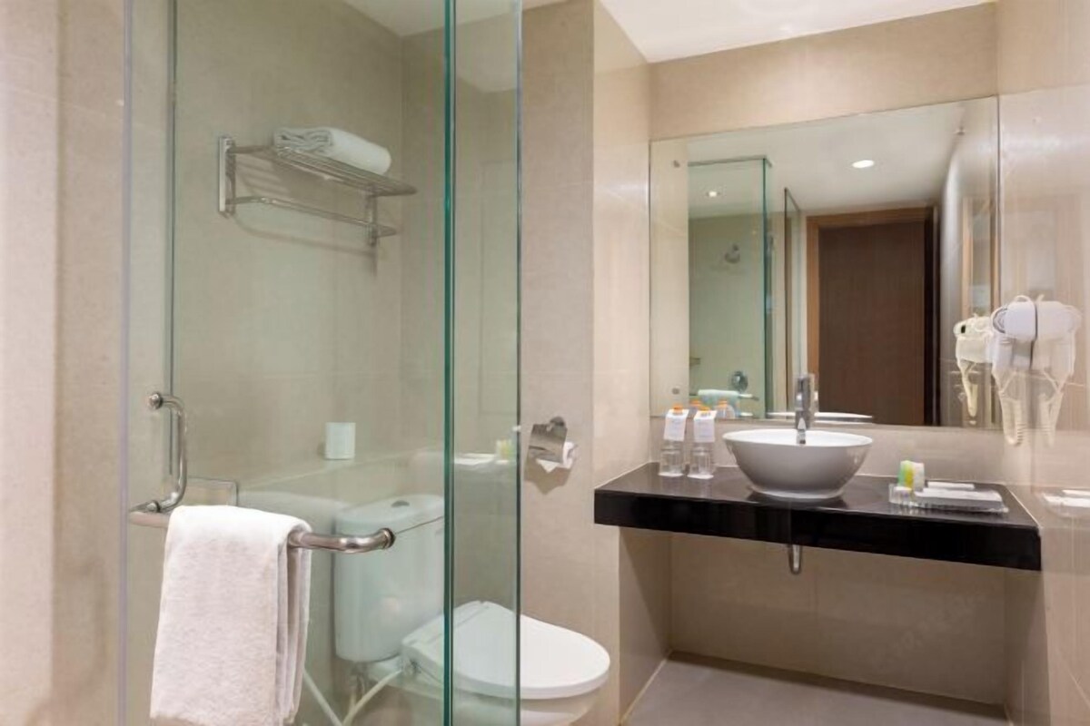 Une salle de bain moderne avec une douche à parois de verre, des toilettes blanches, un plan de toilette noir avec un lavabo et un miroir.